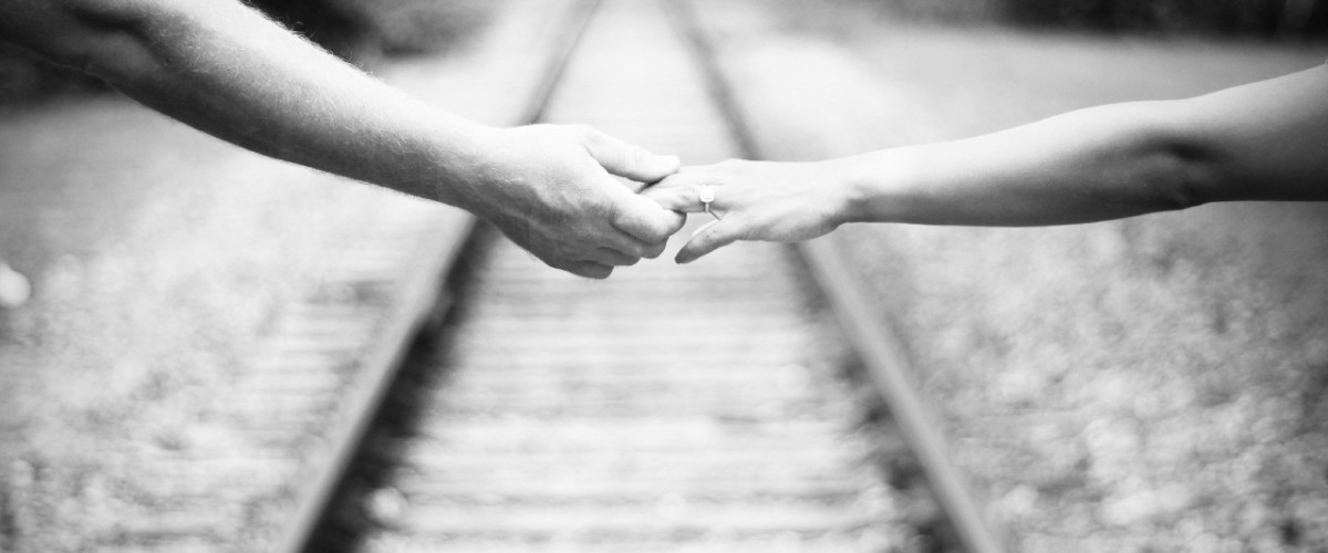 Alt Text: Zwei Hände, die sich auf einer Eisenbahnstrecke halten, symbolisieren Unterstützung.